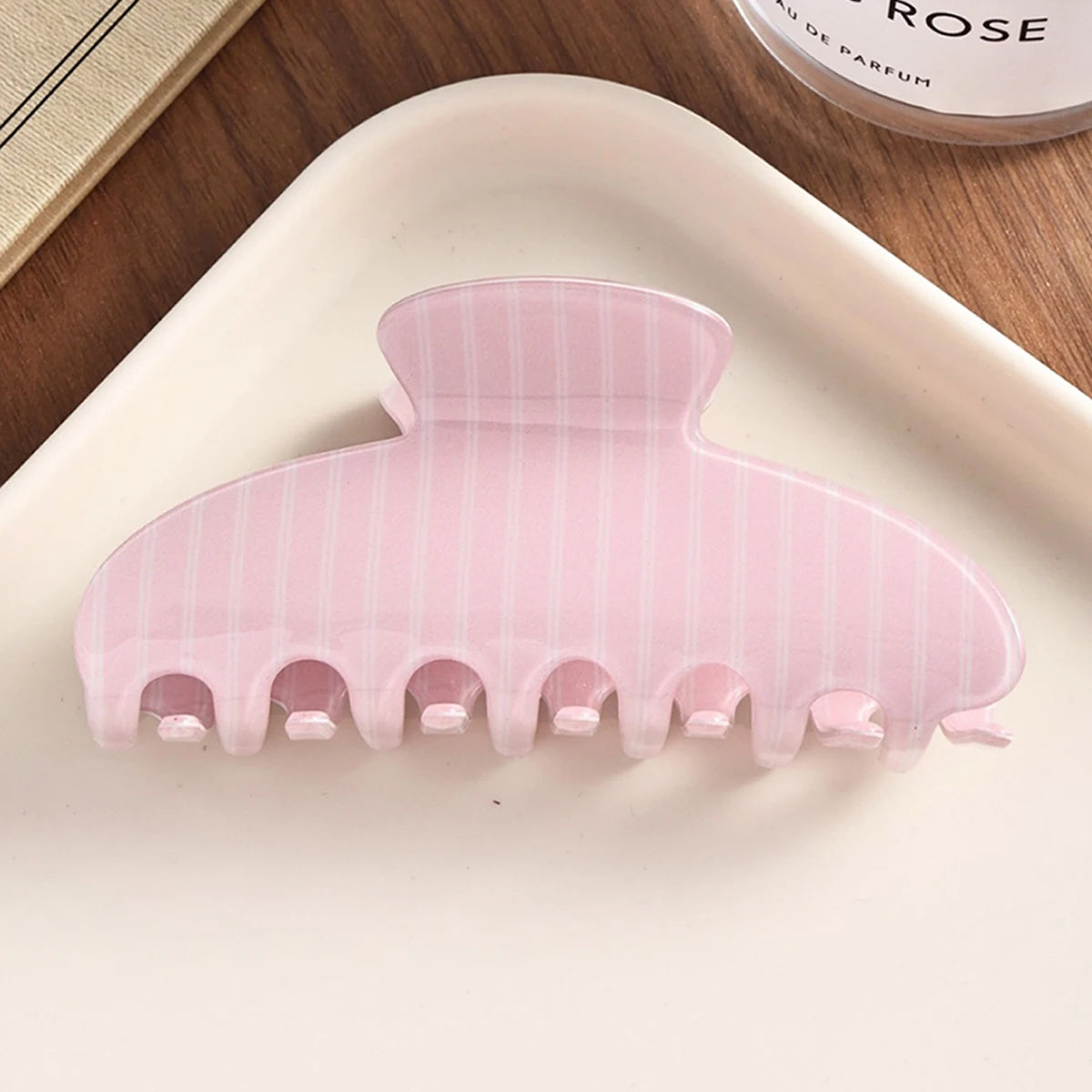A pink striped silicone hair clip is displayed on a white plate.