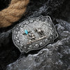 Boucle de ceinture en métal argenté avec une scène détaillée d'un cheval et d'un cavalier sur une surface de pierre sombre.