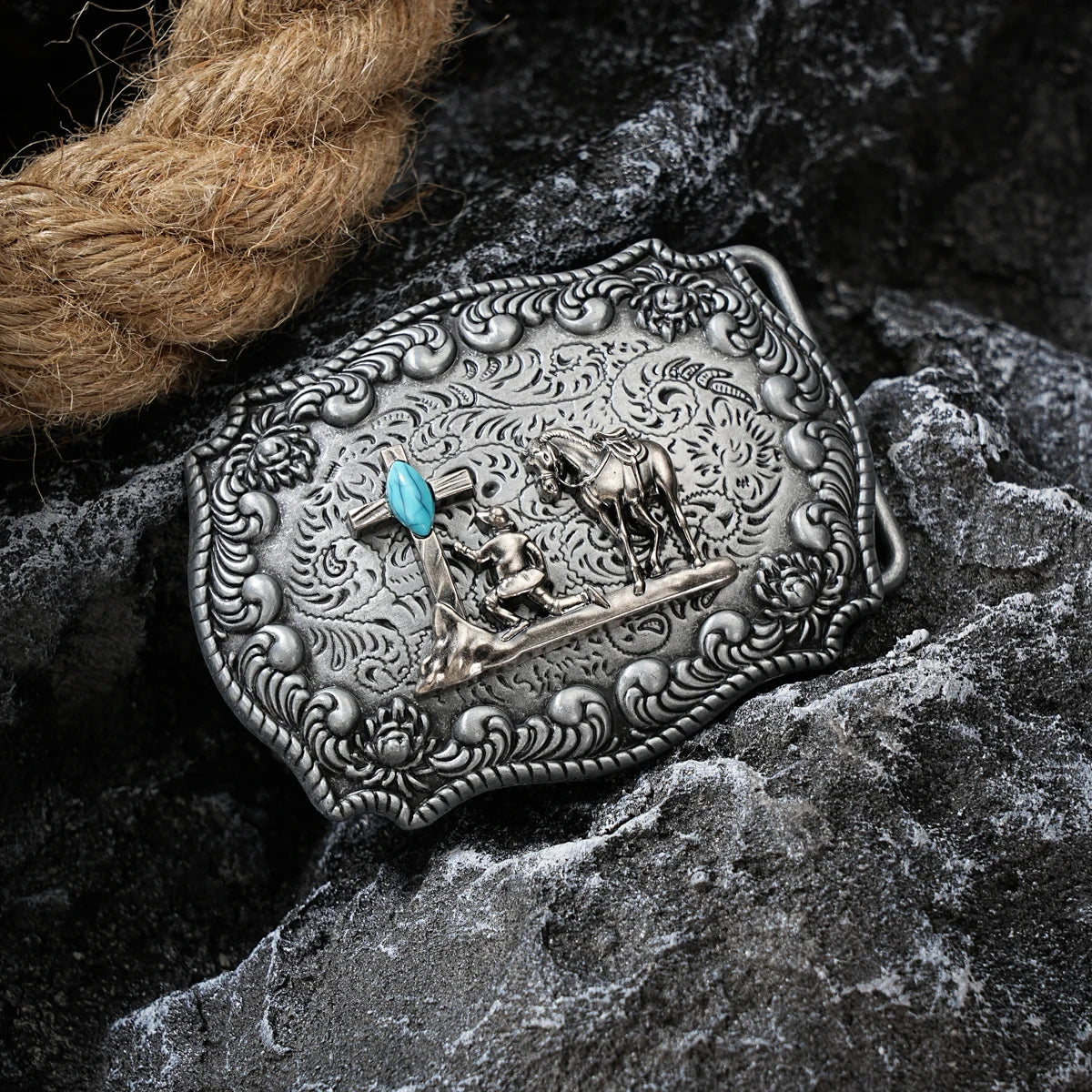 Boucle de ceinture en métal argenté avec une scène détaillée d'un cheval et d'un cavalier sur une surface de pierre sombre.