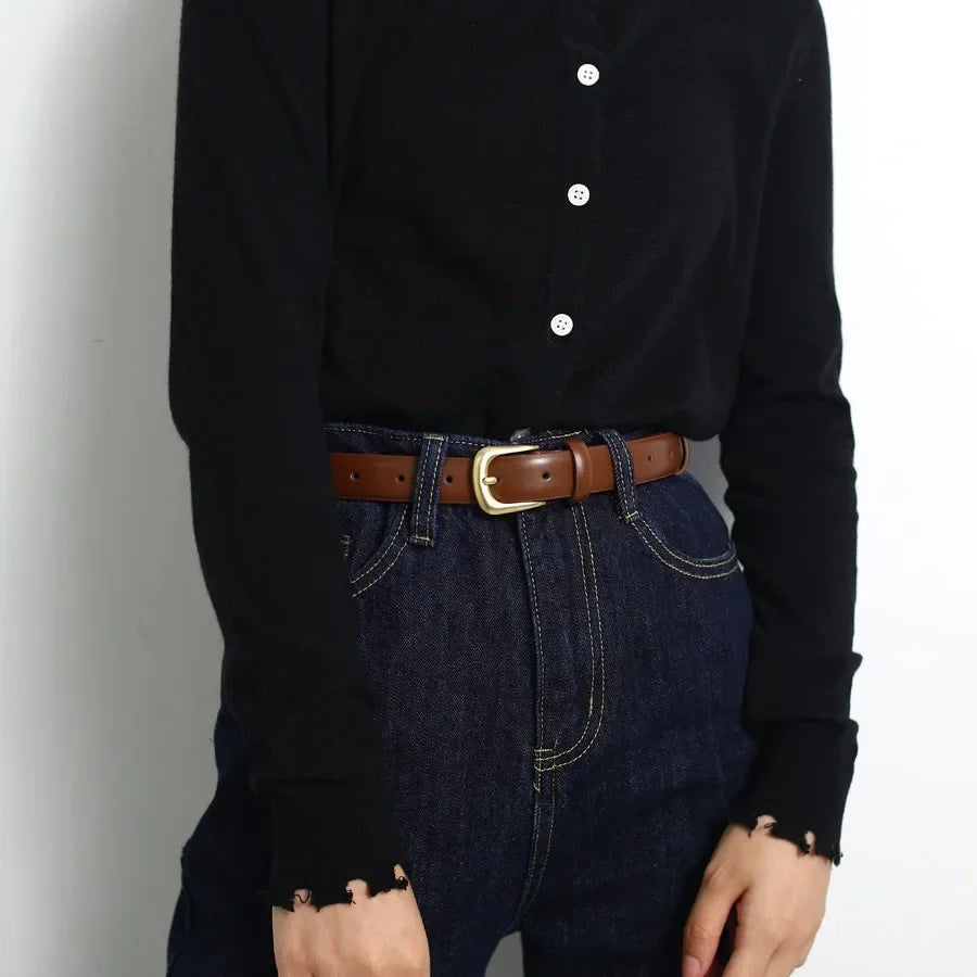 A close-up of a brown leather belt worn with dark blue denim jeans and a black long-sleeved shirt.