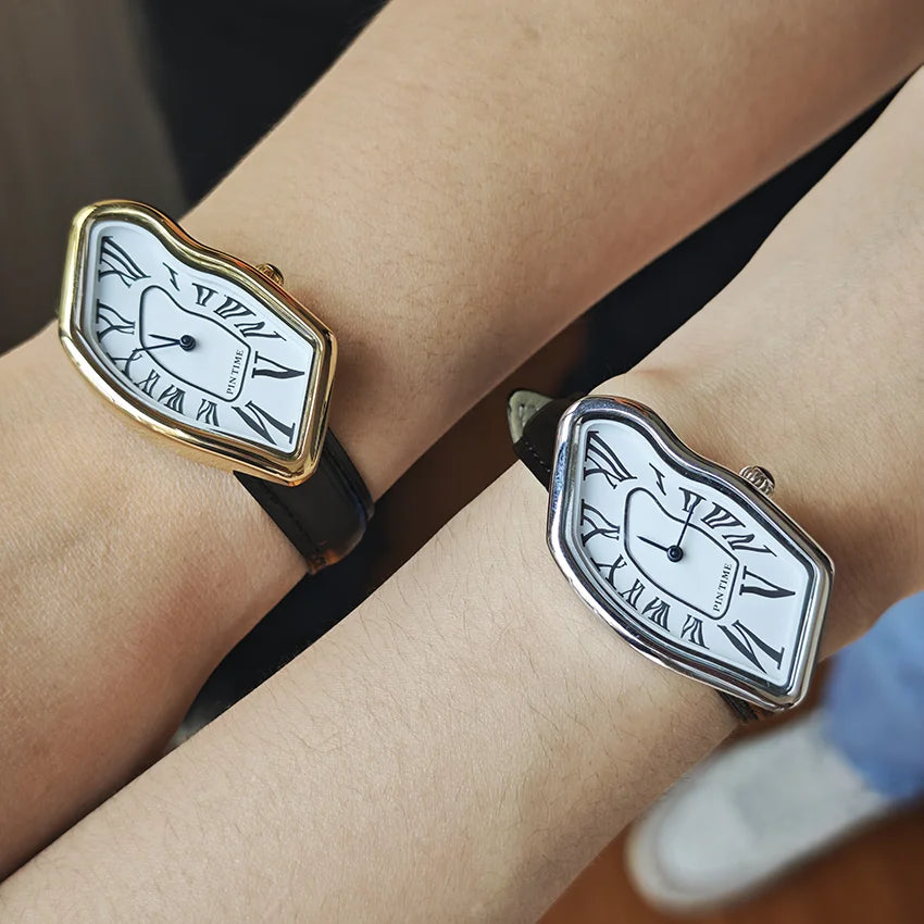 A close-up of a vintage irregular quartz watch with a gold-toned bezel and white face on a person's wrist.