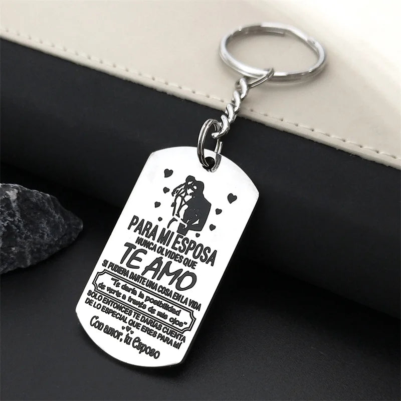 A silver stainless steel tag with a silhouette of a couple and text in Spanish hangs from a keyring.