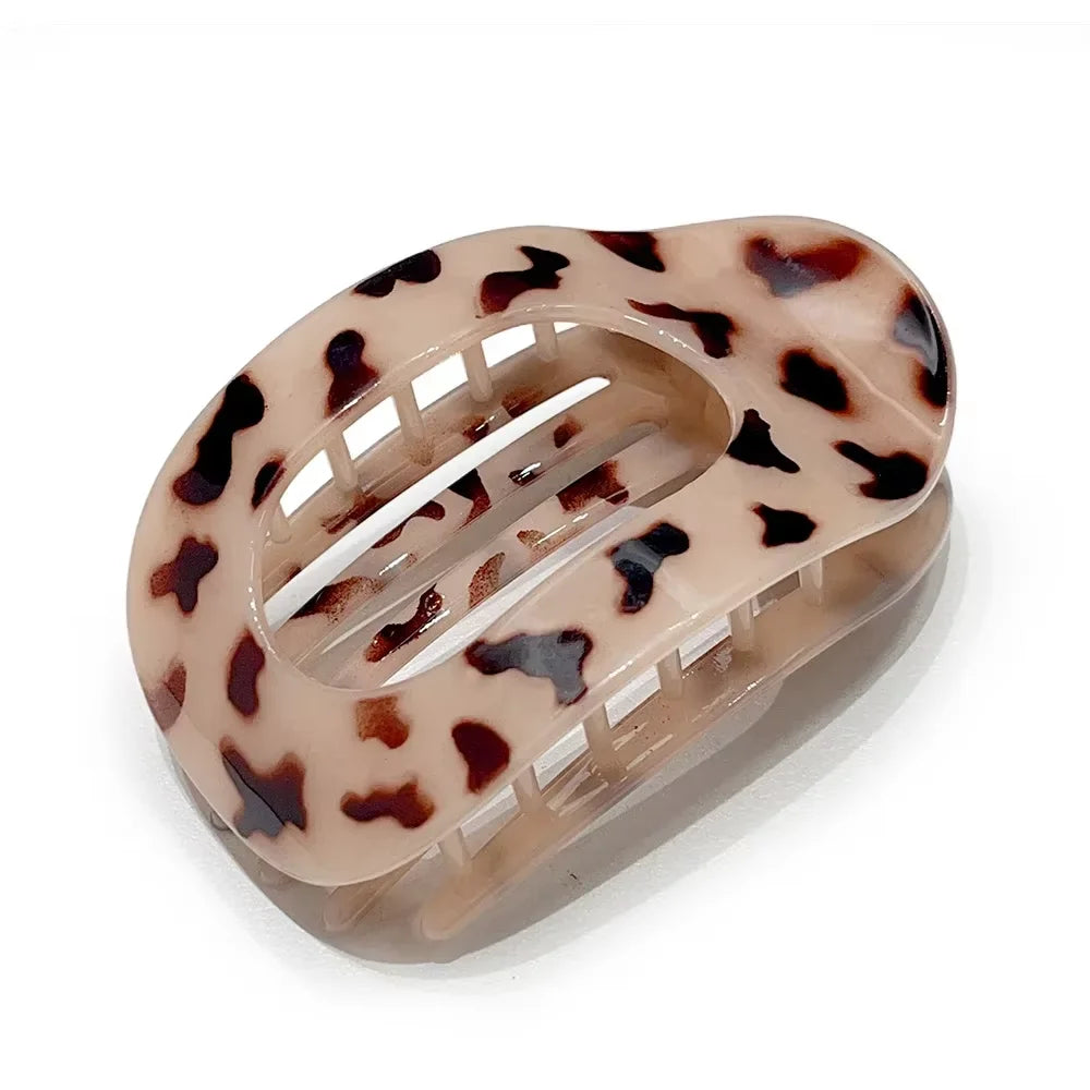 A matte oval hair claw clip featuring a leopard print pattern in shades of brown and beige.