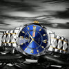 A close-up shot of a stainless steel watch with a blue dial and gold accents resting on a dark, reflective surface.