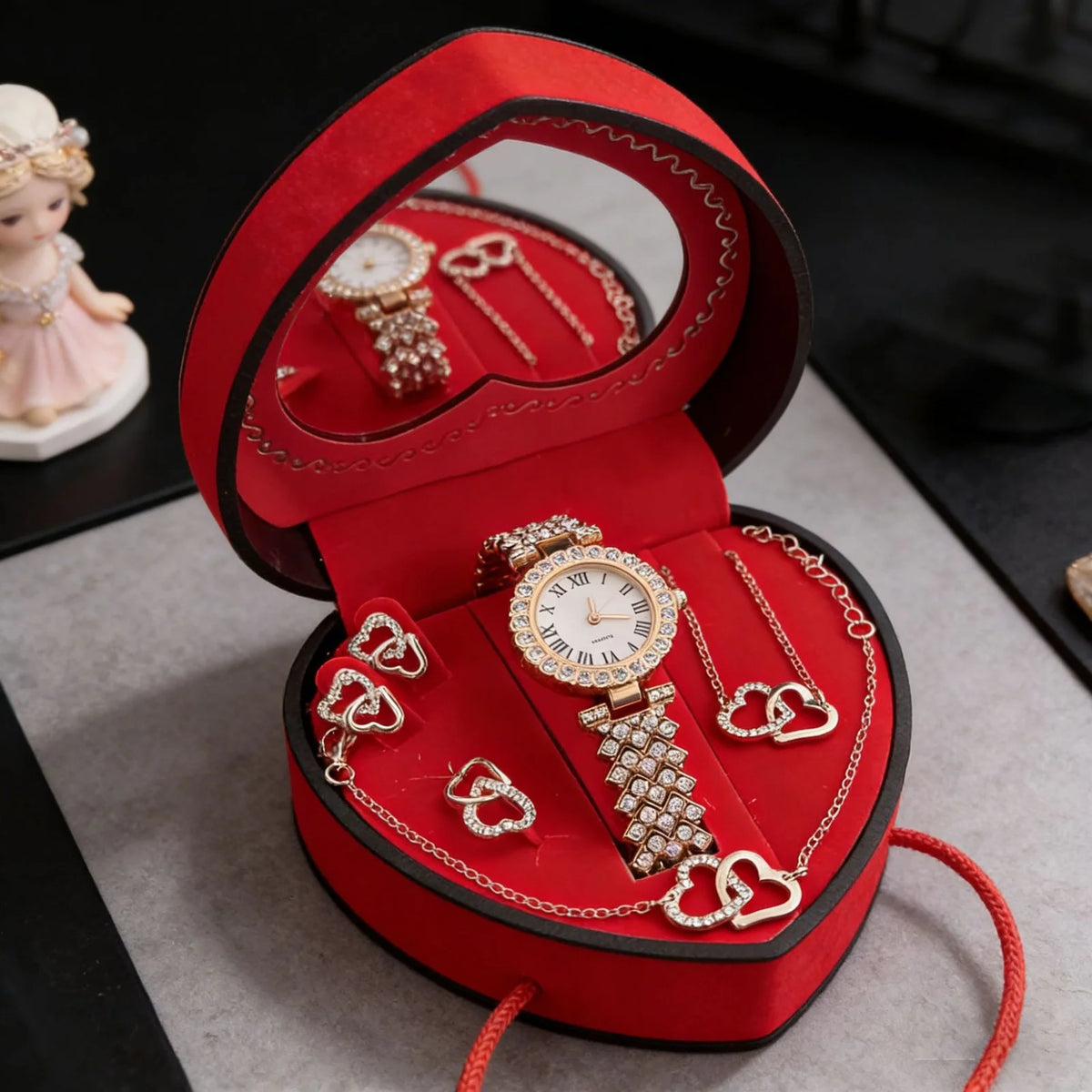 A red velvet jewelry box containing a gold watch and various rhinestone heart-shaped necklaces and earrings.
