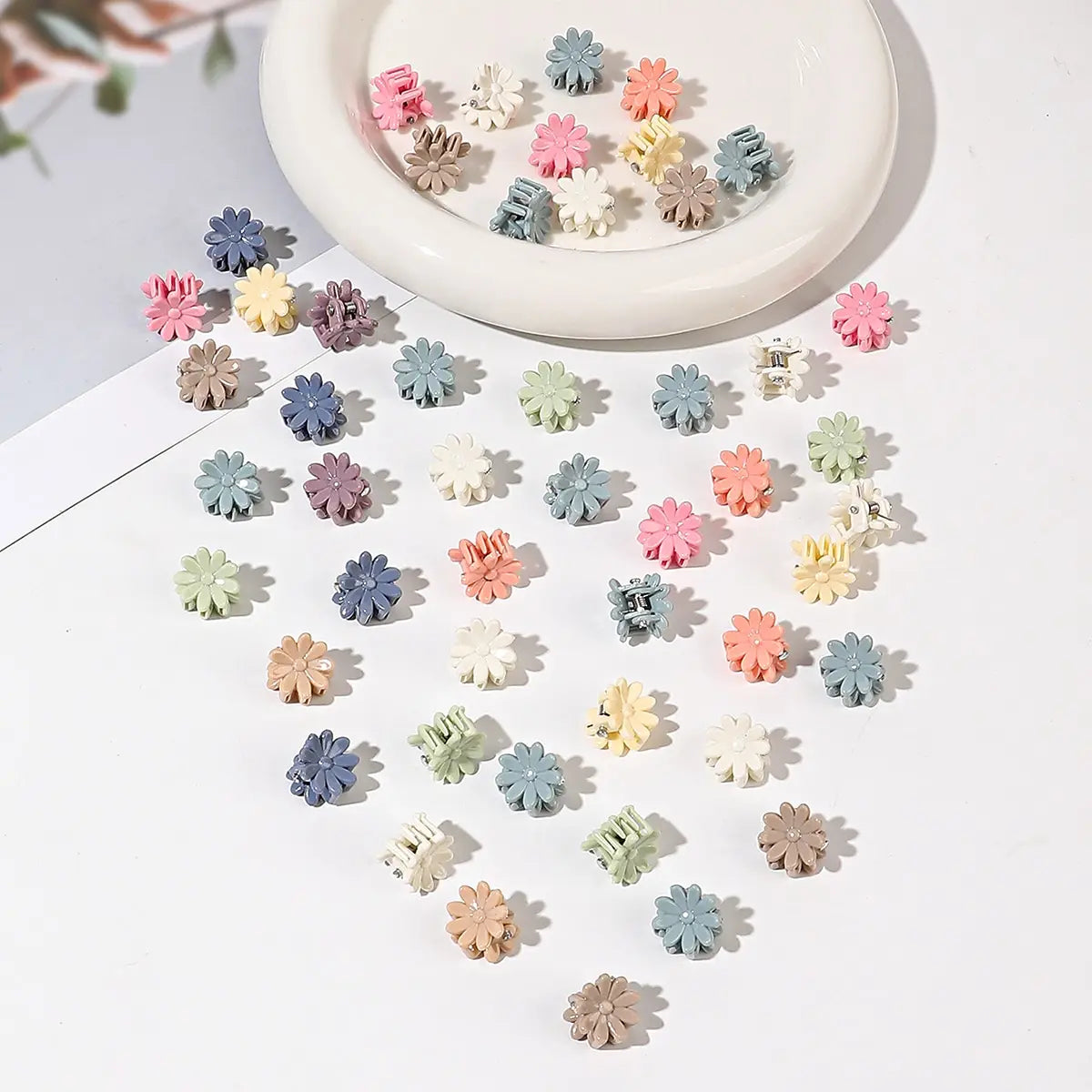 A collection of colorful mini flower hair clips in various pastel shades scattered on a white surface.