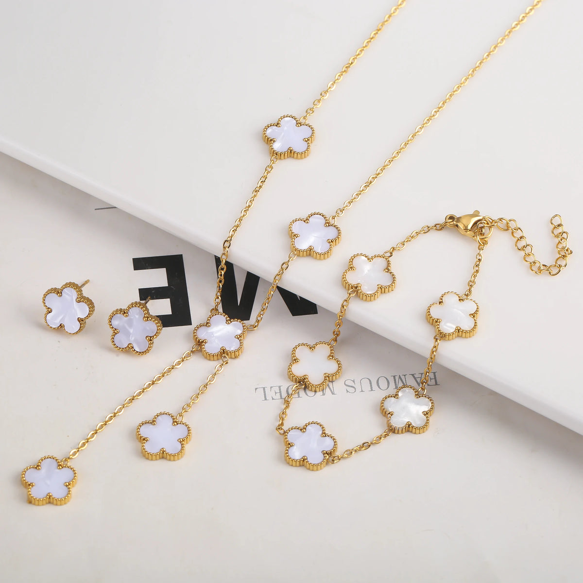 Pulsera de flor de acero inoxidable chapado en oro con pequeños adornos florales blancos en una cadena delicada.