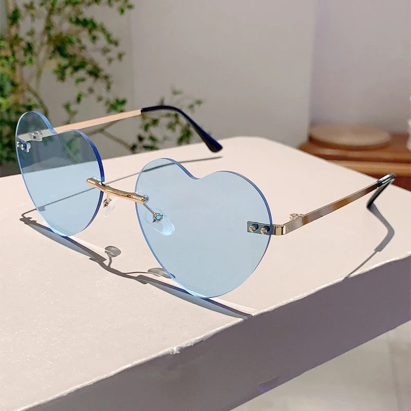 Vintage Herzform-Sonnenbrille ohne Rand mit hellblauen Linsen und goldfarbenen Metallrahmen auf weißem Untergrund.