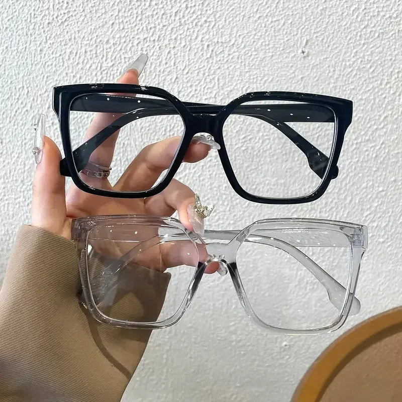 Una mano sostiene un par de gafas cuadradas negras y un par de gafas rectangulares transparentes.