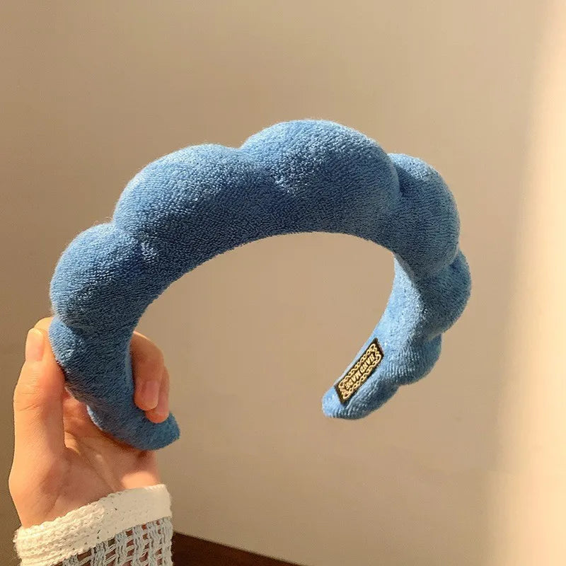 A hand holds a blue cloud-shaped sponge hair accessory headband.