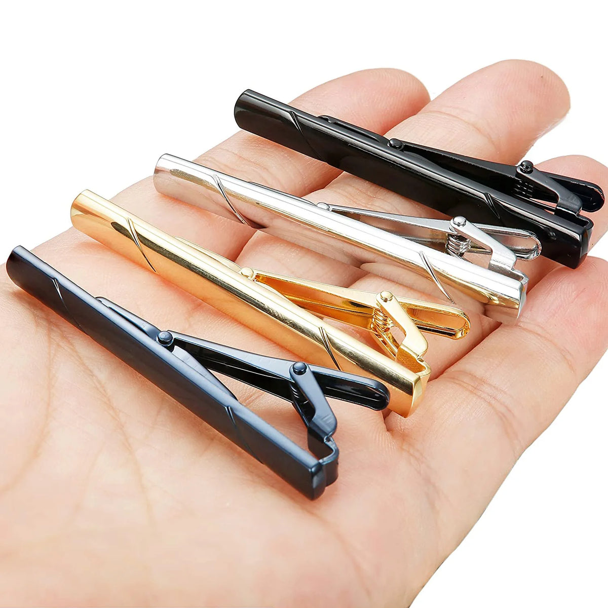 A hand holds four different styles of 14K copper tie clip jewelry in black, silver, and gold finishes.