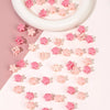 A collection of pink and coral mini flower hair clips arranged on a white plate.