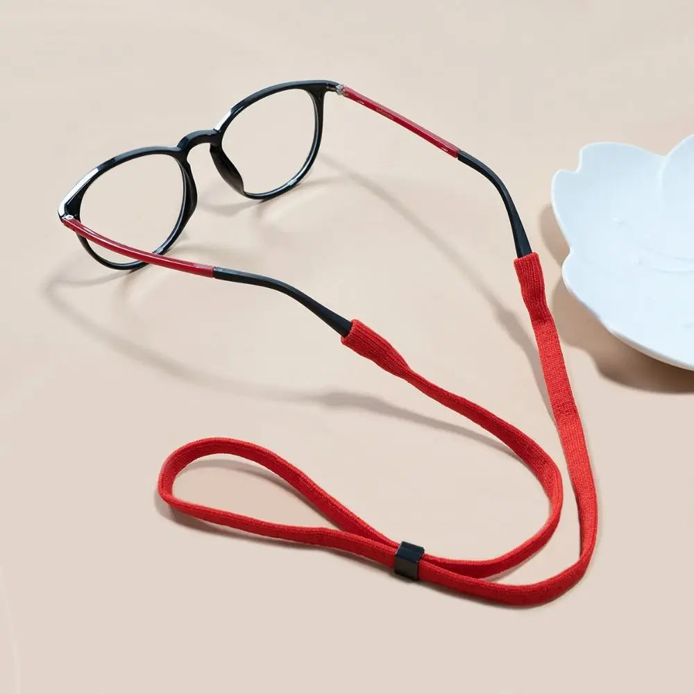 A pair of black eyeglasses with a red lanyard is displayed on a light background.