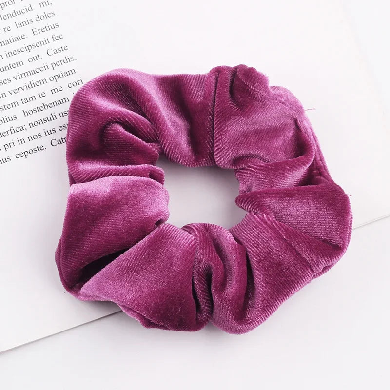 A close-up of a deep purple velvet scrunchie with gathered fabric texture.