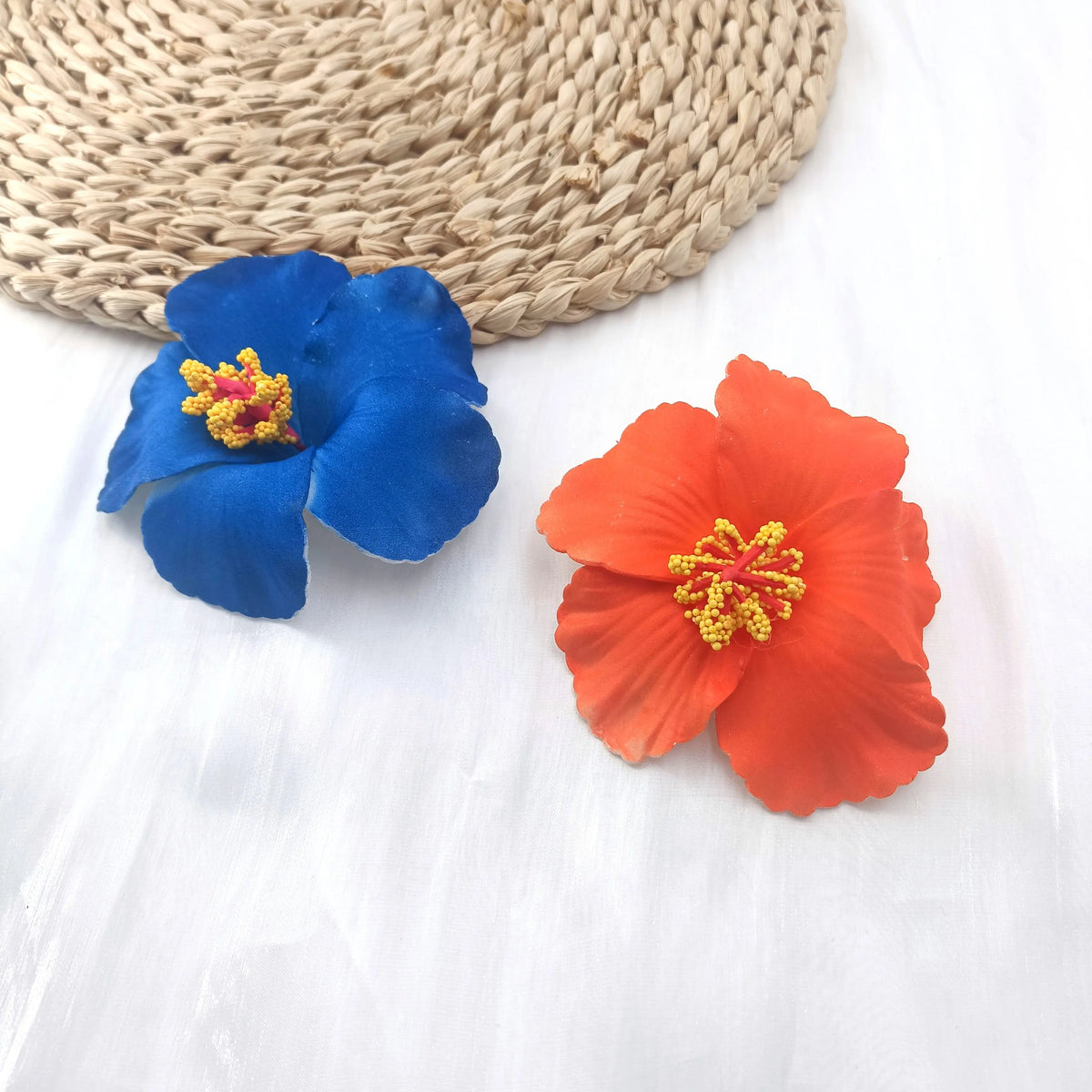 A set of delicate blue and orange floral fabric flowers resting on a woven mat.