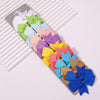 A collection of colorful handmade ribbon bow hair clips in various shades of pink, purple, green, and blue arranged on a stri