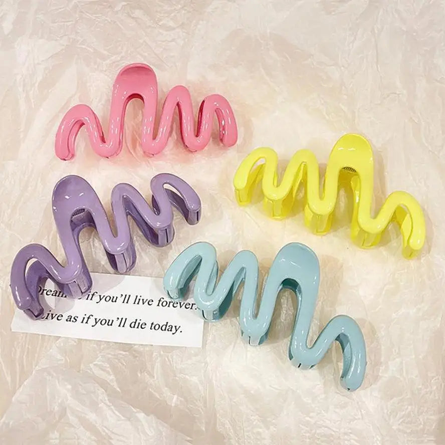 Una colección de pinzas para el cabello tipo ola de gelatina de colores en rosa, morado y amarillo exhibidas sobre una superf