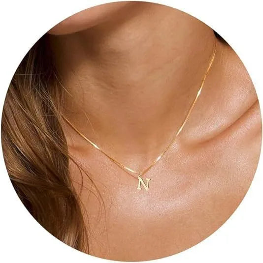 A close-up of a gold plated alphabet initial necklace worn around the neck against skin.