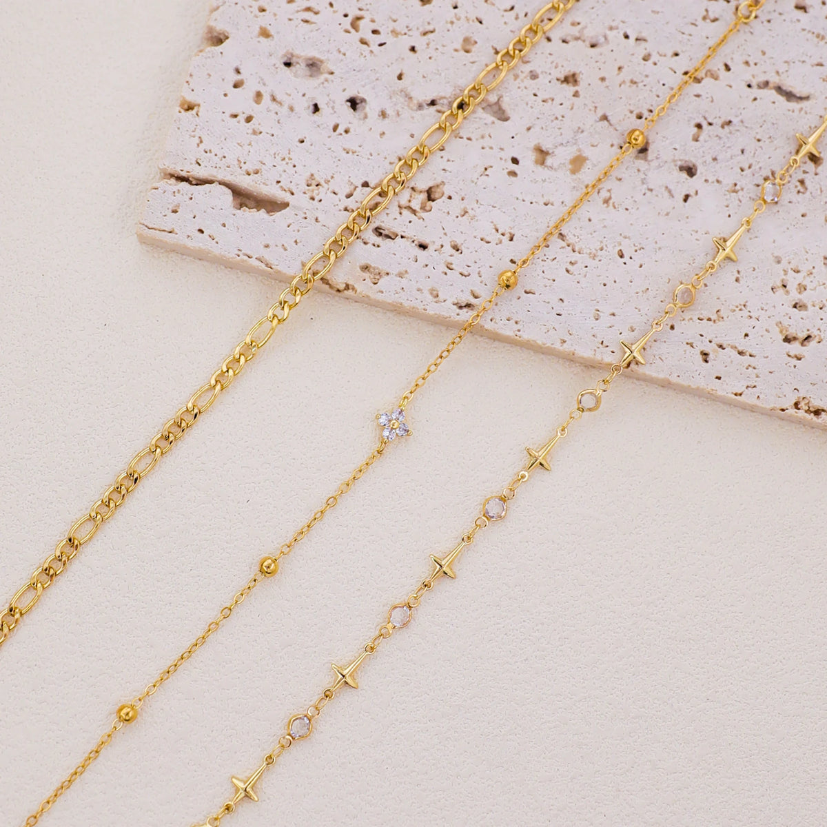 A set of delicate gold-toned crystal cross anklets displayed on a light background.