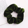 A close-up shot of a dark olive green velvet scrunchie resting on a white background.