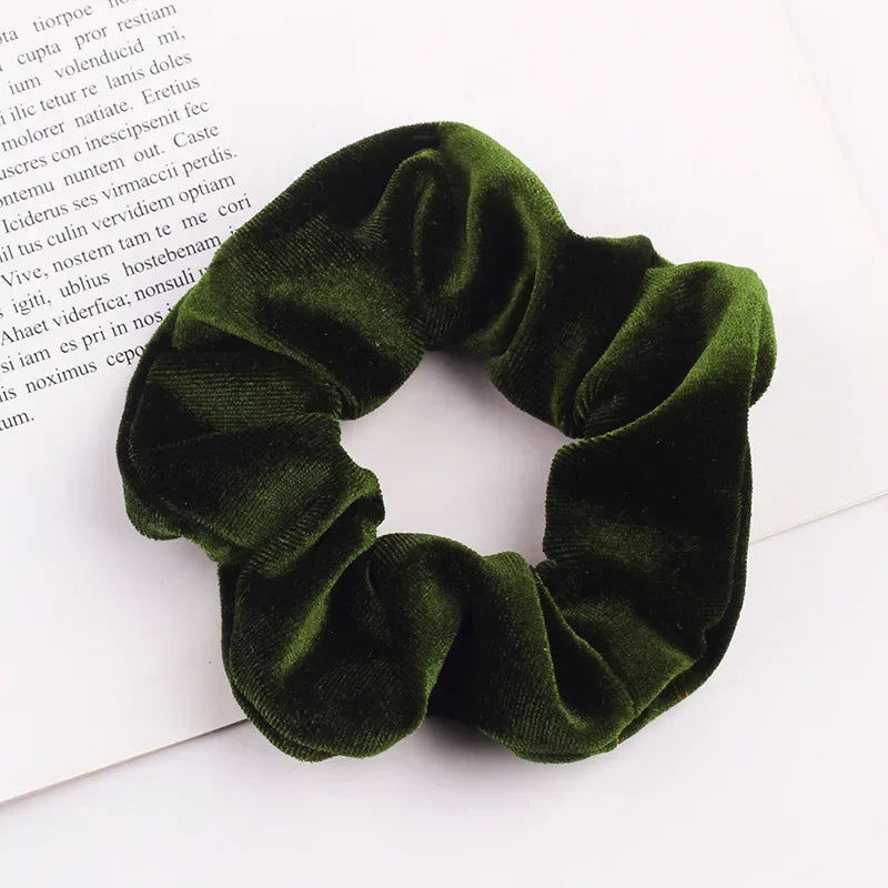 A close-up shot of a dark olive green velvet scrunchie resting on a white background.