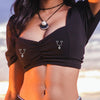 A woman wearing a black cropped top featuring heart dangle non-piercing nipple rings with cubic zirconia.
