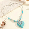 Collier de perles argentées et turquoise avec pendentif en forme de cœur sur fond clair.