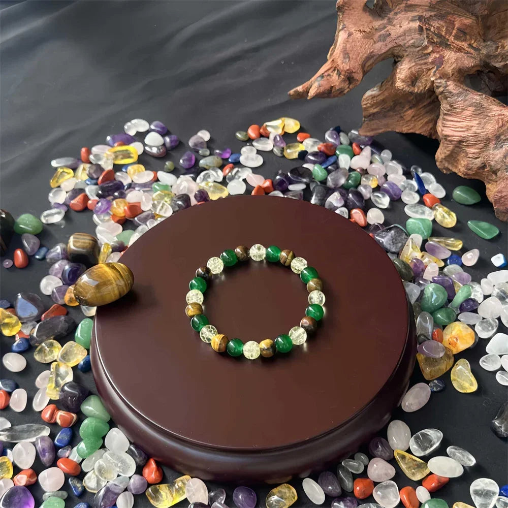 A natural stone and wooden bead prosperity bracelet displayed on a dark brown wooden base surrounded by various colorful ston