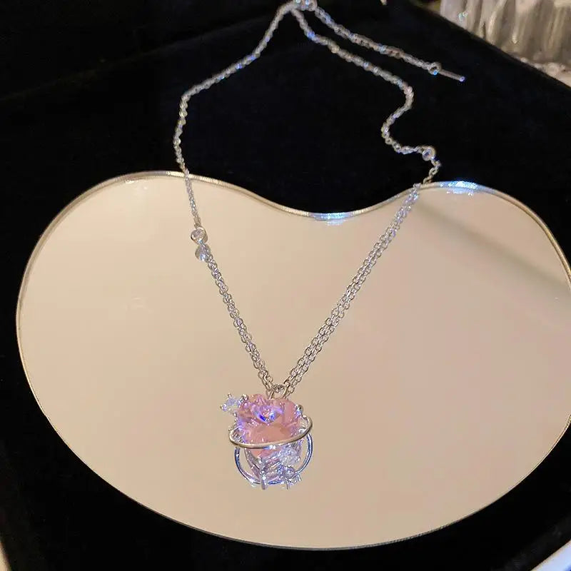 A delicate silver heart necklace featuring a pink zircon gemstone and surrounding clear stones.