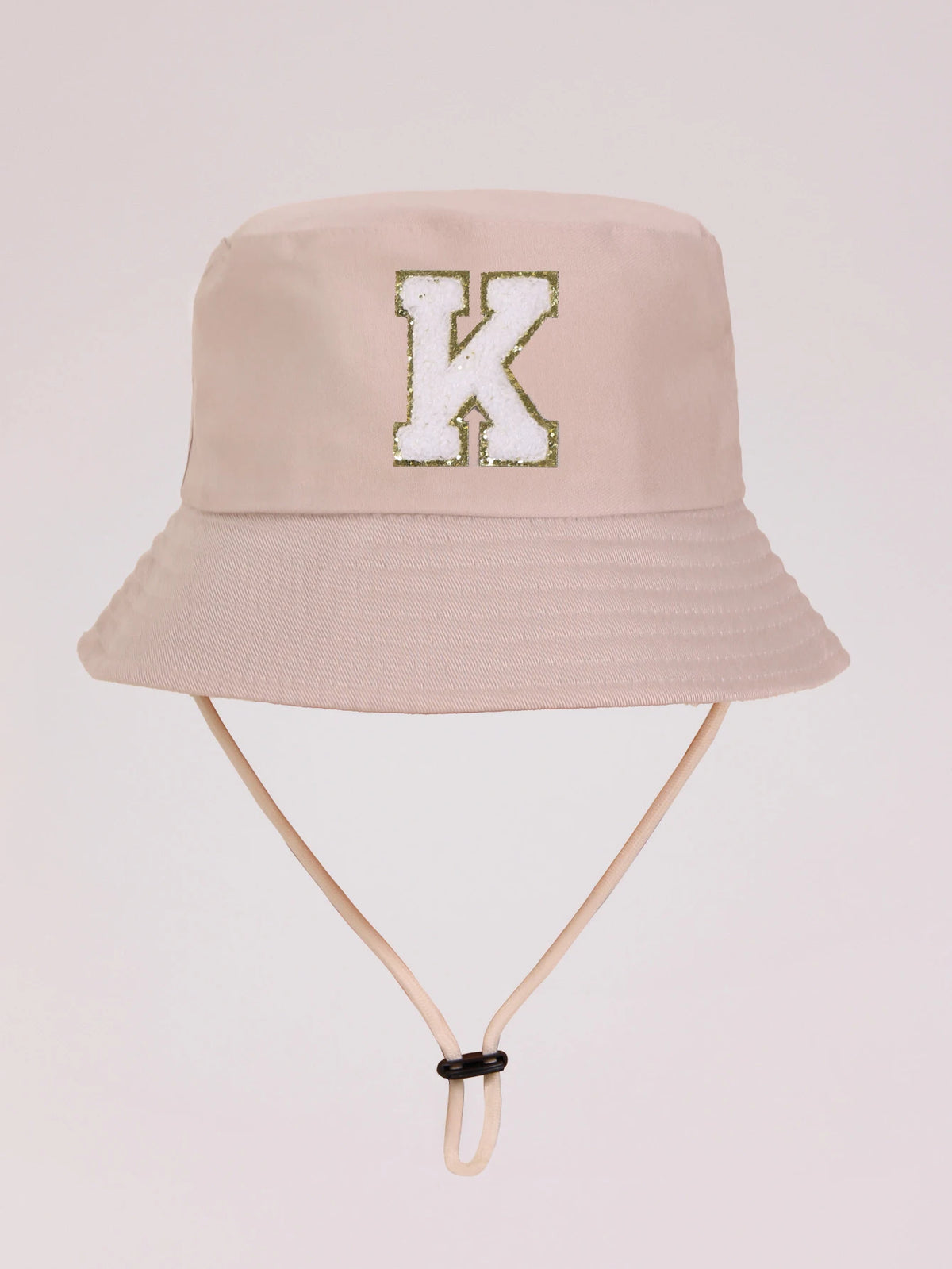 A light beige sun hat with a gold letter K embroidered on the front and a light tan strap.
