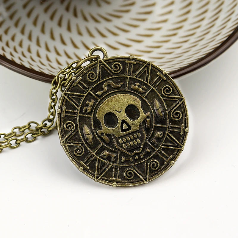 A round brass skull pendant necklace with an intricate design and chain, set against a white background.