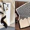 A black and white chevron patterned silk scarf draped on a white card against a beige background.