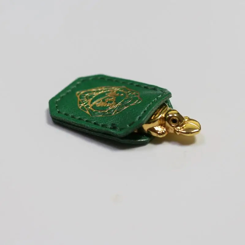 A green leather charm shaped like a turtle with a gold design, used for longevity and financial stability.