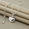 A silver heart snake necklace is displayed on a beige fabric background.