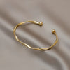 A minimalist gold-tone twisted cuff bangle resting on a neutral fabric background.