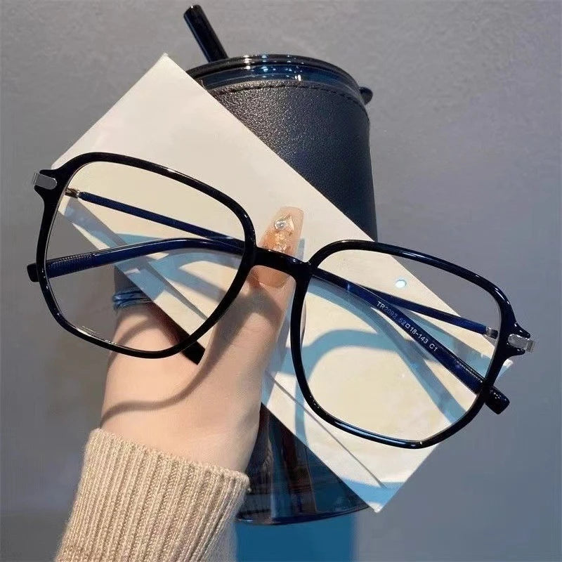 A pair of black retro anti-blue light sunglasses resting on a white paper next to a dark tumbler.