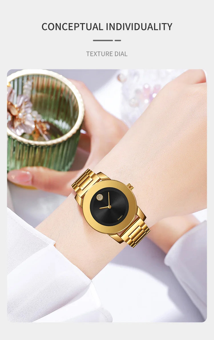 A gold-toned minimalist quartz wristwatch is shown on a wrist next to a textured green cup.