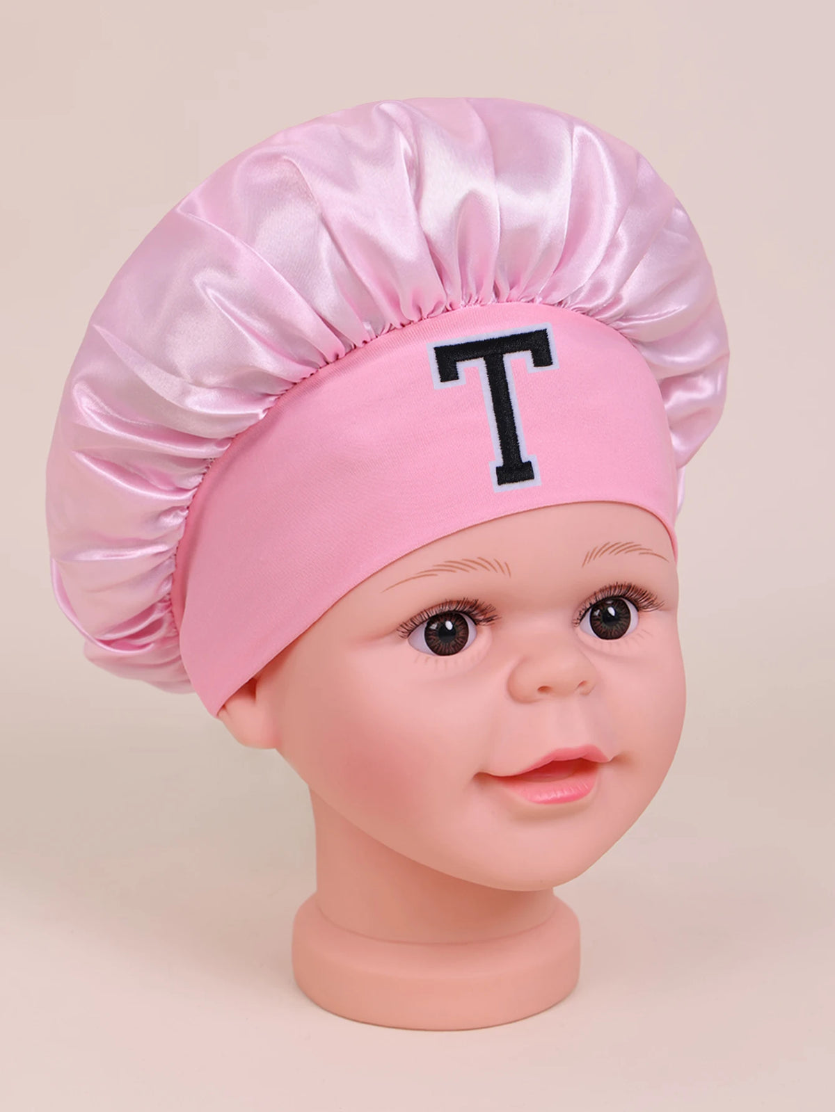 Pink satin sleep cap with a large black letter T on a baby doll head