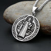 Silver pendant necklace featuring a detailed Saint Benedict exorcism design on a round disc, resting on a smooth stone.