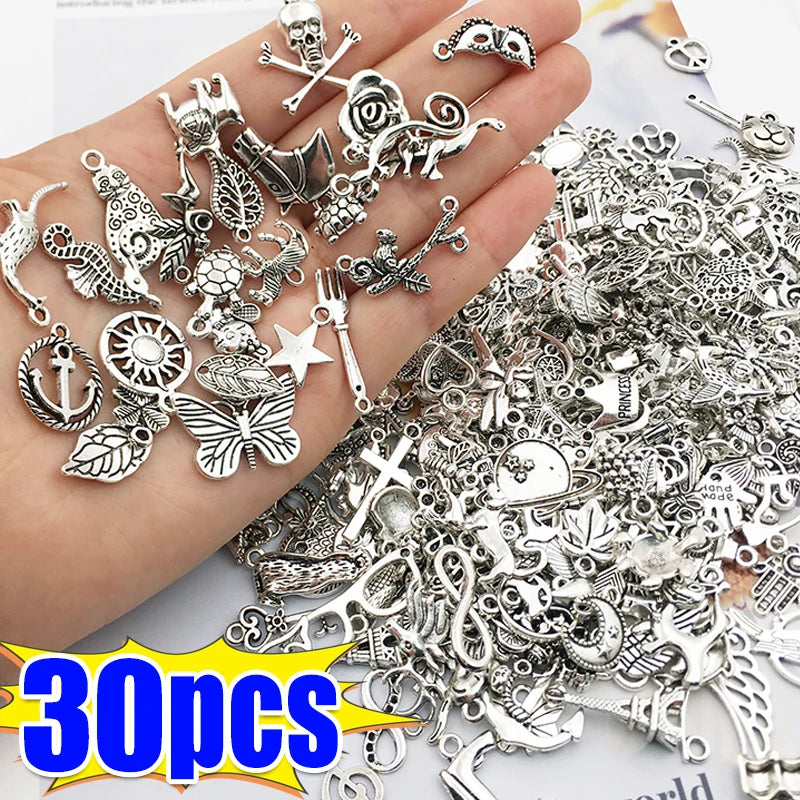 Eine Hand hält eine Sammlung silberner tibetischer Mix-Anhänger und verschiedener Schmuckbauteile für DIY-Bastelarbeiten.