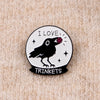 Silueta negra de un pájaro con una joya roja en la cabeza dentro de una gema circular con el texto I LOVE y TRINKETS