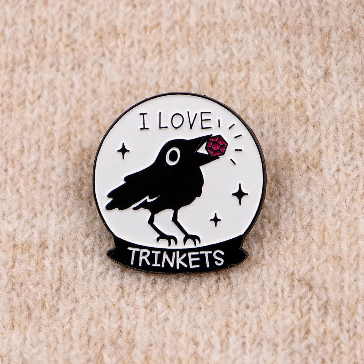 Silueta negra de un pájaro con una joya roja en la cabeza dentro de una gema circular con el texto I LOVE y TRINKETS