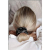 A close-up of a woman's blonde hair styled in a neat ponytail using a black silk scrunchie.