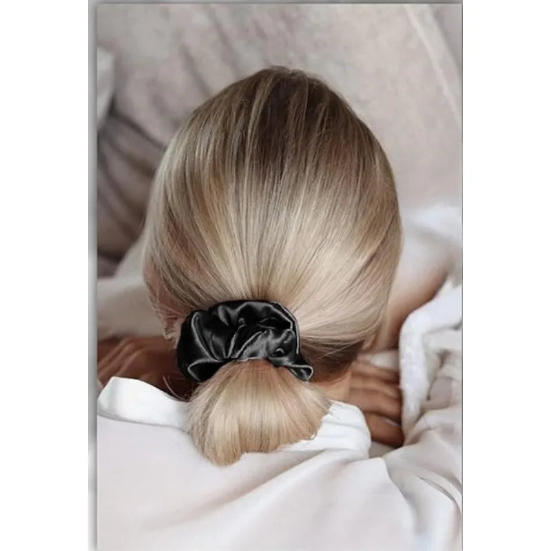 A close-up of a woman's blonde hair styled in a neat ponytail using a black silk scrunchie.