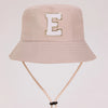 A beige sun hat with a gold letter E embroidered on the front and a light beige strap.