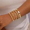 A hand wearing a stack of four gold-plated chunky cuff bangles on the wrist.