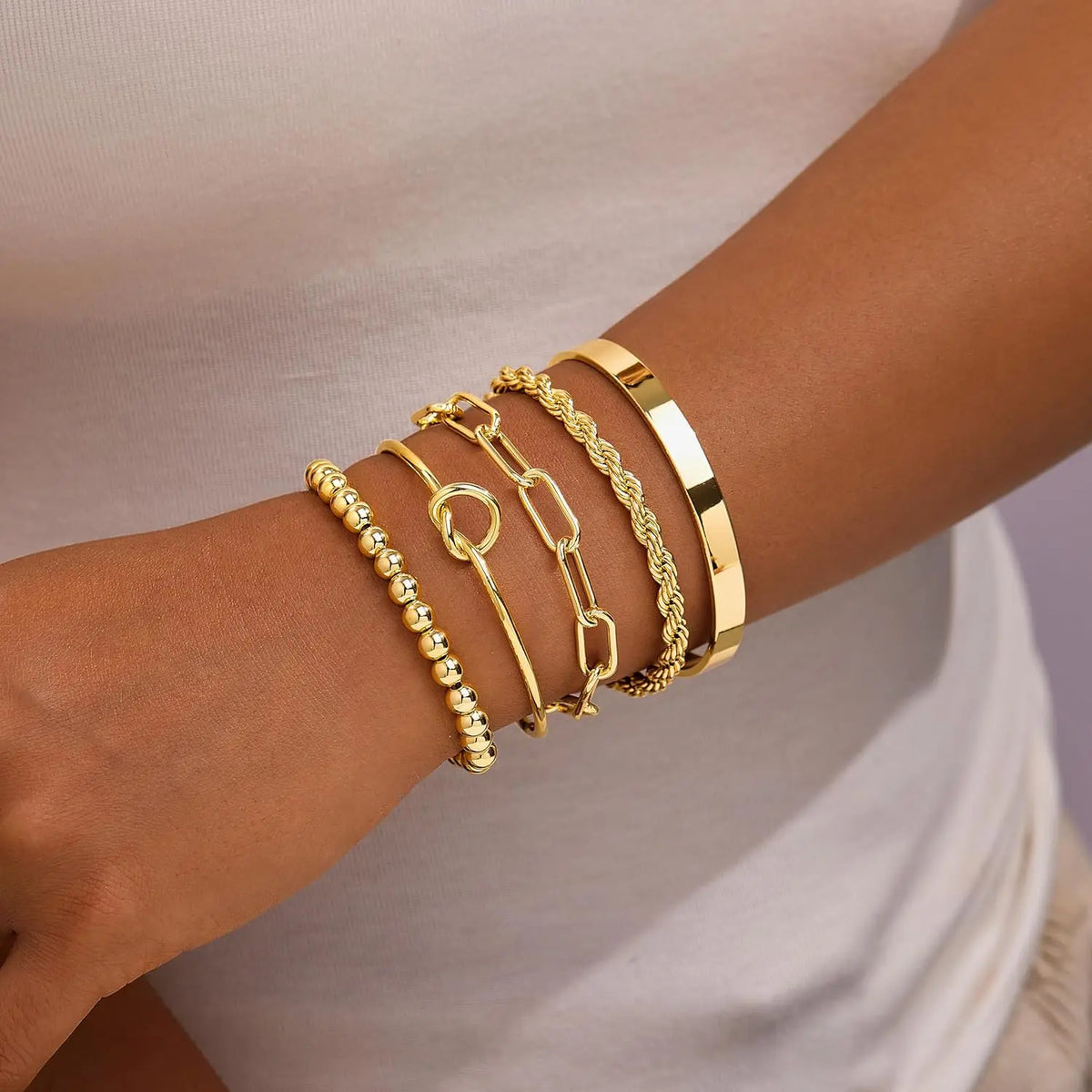 A hand wearing a stack of four gold-plated chunky cuff bangles on the wrist.