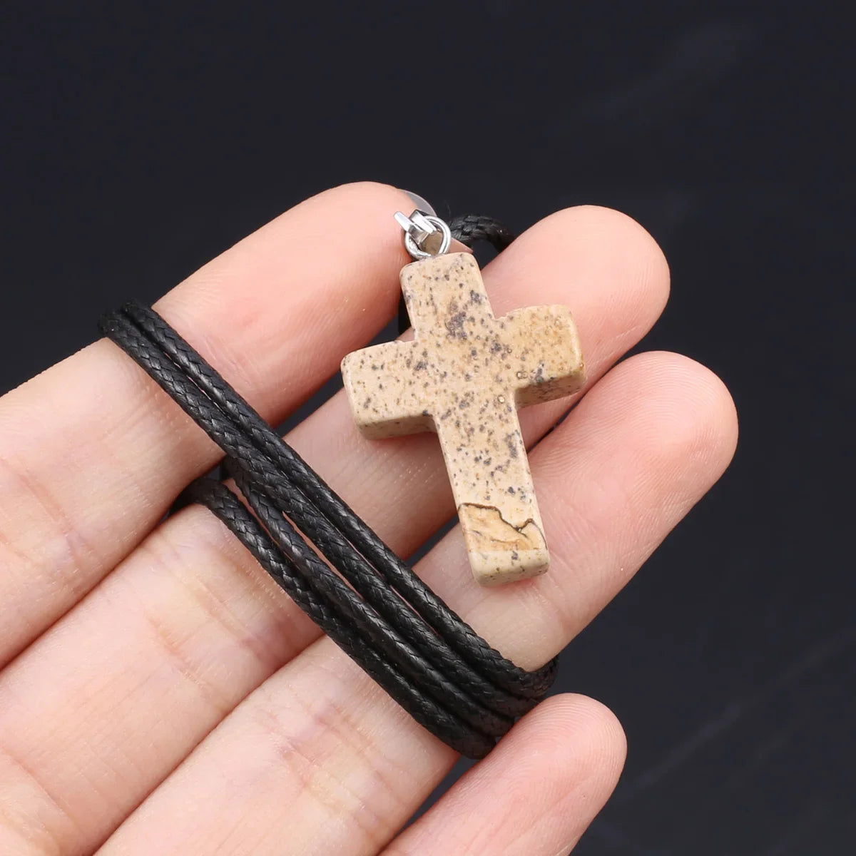 Eine Hand hält eine Tigerauge-Achat-Kreuz-Anhängerkette vor einem dunklen Hintergrund.