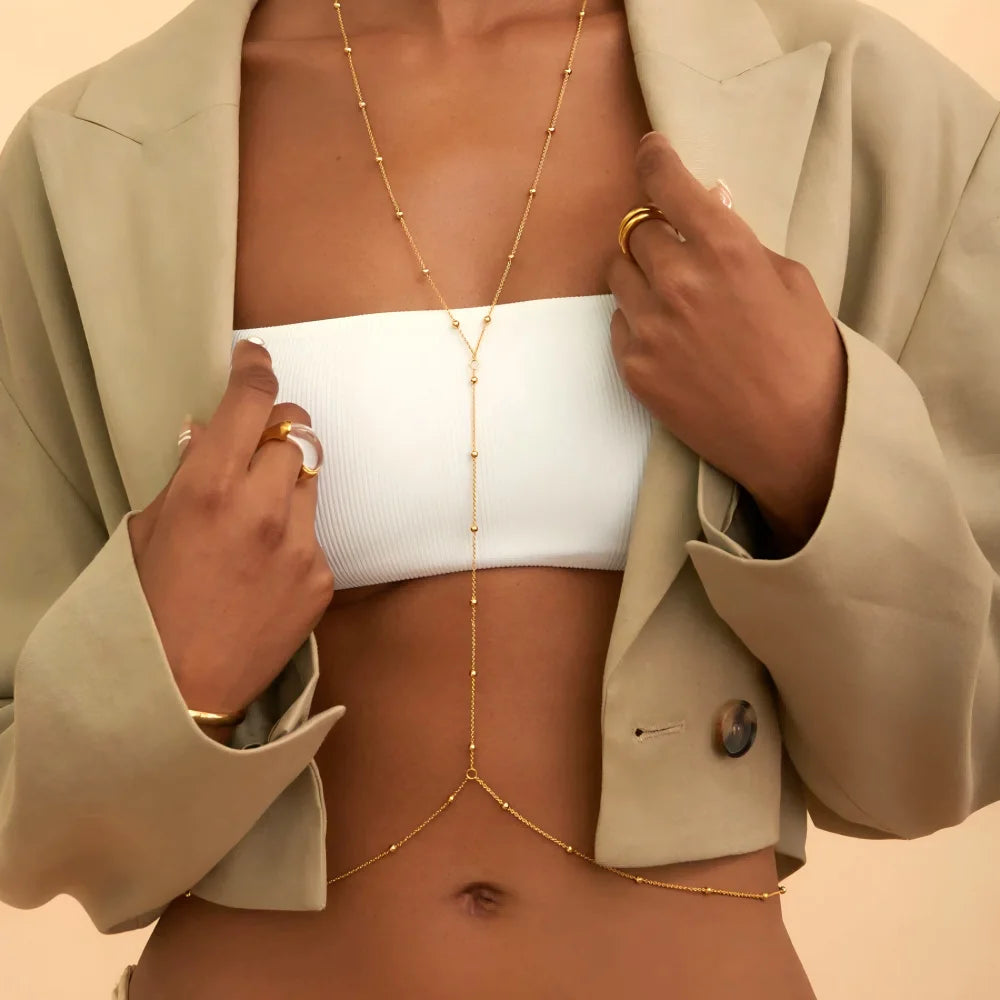 A close-up of a woman wearing a gold adjustable belly chain body jewelry over a white top and beige blazer.