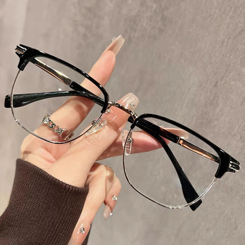 Eine Hand hält eine schwarze Anti-Blaulicht-Lesebrille mit dünnen goldenen Akzenten vor grauem Hintergrund.